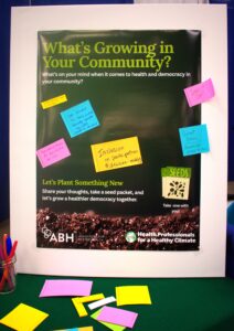 ABH and HPHC's tabling poster with sticky notes from conference attendees. The sign has the tagline: What's growing in your community with let's plant something new. Share your thoughts, take a seed packet, and let's grow a healthier democracy together.