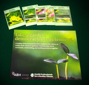 HPHC and ABH's table materials. Seed packets and a sign with the tagline: "Like a garden, democracy needs tending" with ABH and HPHC's logos.