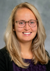 Ashley, a young person with blonde hair and light skin tone wears brown acetate textured glasses and a black top.